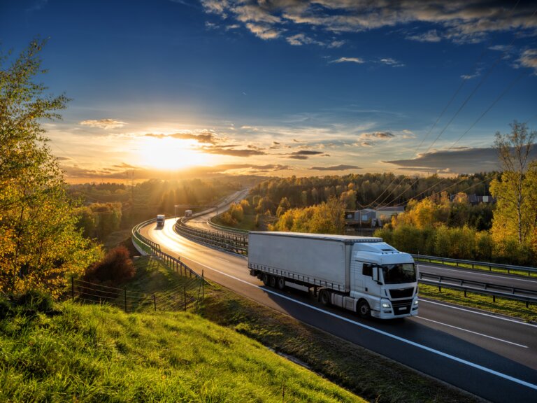 White trucks driving on the highway winding through forested landscape in autumn colors at sunset