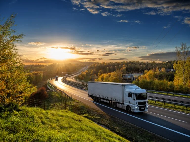 White trucks driving on the highway winding through forested landscape in autumn colors at sunset